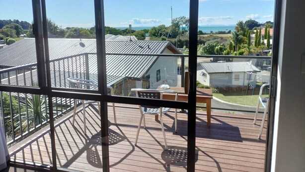 A balcony with a table and chairs, overlooking a residential area with houses and a clear sky. - Two Bedroom Apartment Sea View (Kaiteriteri)