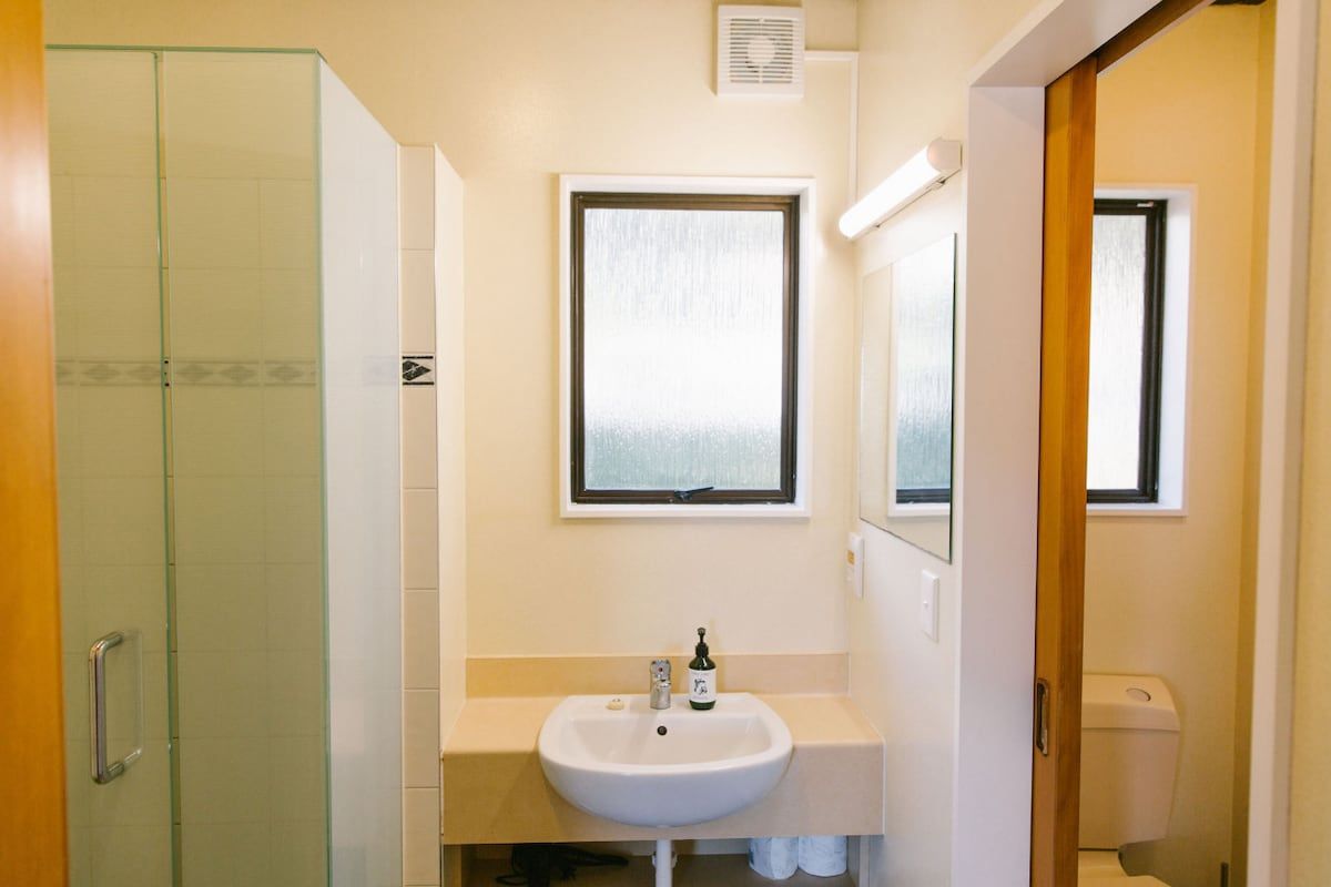 A bathroom with a glass shower enclosure, a white sink with a mirror above it, and a window providing natural light.