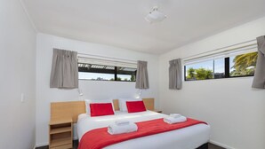 A hotel room with a bed, a nightstand, a window with curtains, and a view of palm trees.