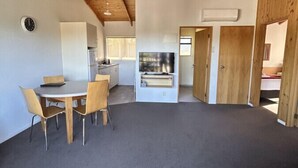 A spacious room with a high ceiling, wooden beams, a dining area with a table and chairs, a television, and a door leading to another room. - Two Bedroom Garden View (Kaiteriteri)