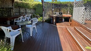 A wooden deck with outdoor seating, a barbecue grill, and a covered area. - Two Bedroom Garden View (Kaiteriteri)