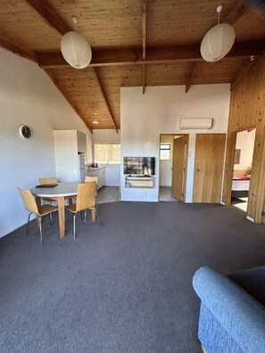 A spacious living area with a dining table and chairs, a sofa, and a kitchen in the background. - Two Bedroom Garden View (Kaiteriteri)