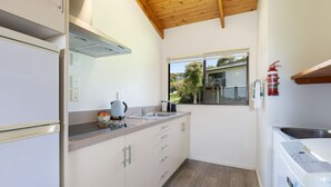 A compact kitchen with a built-in oven, a kettle, and a coffee maker on the countertop. - Two Bedroom Garden View (Kaiteriteri)