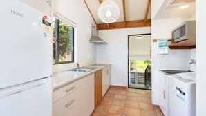 A compact kitchen with a Haier refrigerator, a sink, and a microwave. There is a window providing natural light and a view of the outdoors. - Superior Two Bedroom Sea View (Kaiteriteri)