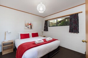A hotel room with a bed, a window with curtains, a bedside lamp, and a wall-mounted artwork. - Cosy Compact - Comfortable 2-Bedroom (Kaiteriteri)