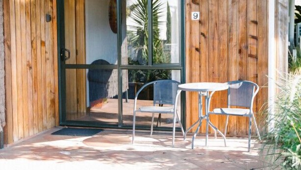 Une façade en bois avec une porte en verre, une terrasse avec un sol carrelé et des chaises en métal.