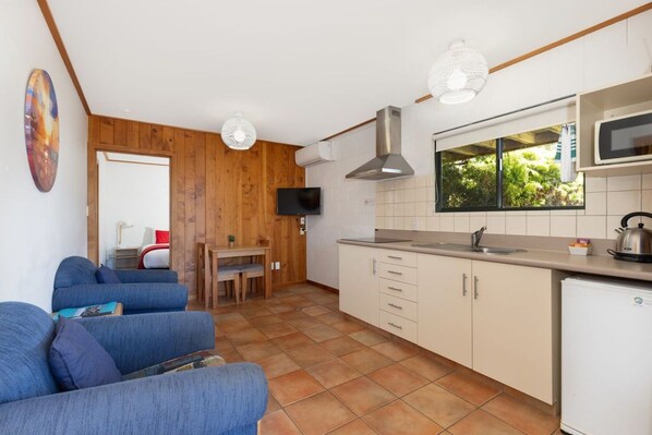 A compact kitchen with a dining area, wooden walls, and a television. - Cosy Compact - Comfortable 2-Bedroom (Kaiteriteri)