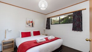 Une chambre d’hôtel bien rangée, avec un grand lit, une table de chevet avec une lampe, une fenêtre avec des rideaux et un tableau accroché au mur.