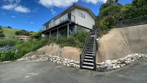A two-story house with a balcony, a staircase leading up to the house, and a stone retaining wall. - Studio Sea View Upper Level (Kaiteriteri)