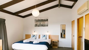 A hotel room with a bed, a bedside table, a lamp, a wall-mounted air conditioner, and a television. - Studio Sea View Upper Level (Kaiteriteri)