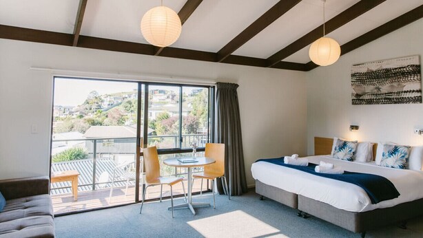 A hotel room with a bed, a dining table with chairs, a sofa, and a view of the outdoors. - Studio Sea View Upper Level (Kaiteriteri)