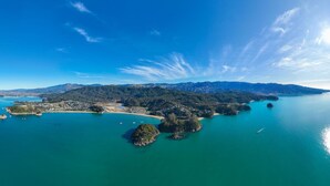 An aerial view of a coastal area with clear blue waters, several small islands, and a distant mountain range. - Budget Studio Unit Garden view (Kaiteriteri)