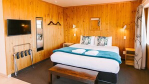 A wooden-paneled room with a bed, a TV, a bench, and a coat rack. - Budget Studio Unit Garden view (Kaiteriteri)