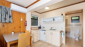A compact kitchen with a dining area, wooden paneling, and a tiled floor. - Budget Studio Unit Garden view (Kaiteriteri)