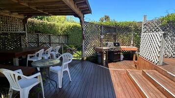 Une terrasse en bois avec des sièges extérieurs, un barbecue et un espace abrité.
