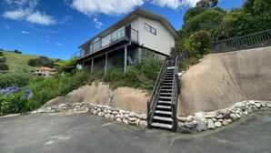 A two-story house with a balcony, a stone retaining wall, and a staircase leading up to the entrance. - Studio Sea View Upper Level (Kaiteriteri)