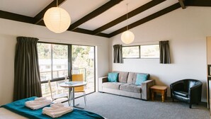 A hotel room with a bed, a sofa, a chair, a small table, and two hanging paper lanterns. - Studio Sea View Upper Level (Kaiteriteri)