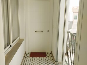 Un couloir étroit avec un sol à motifs, un tapis rouge à l’entrée, une porte avec une poignée et une fenêtre sur le côté gauche.