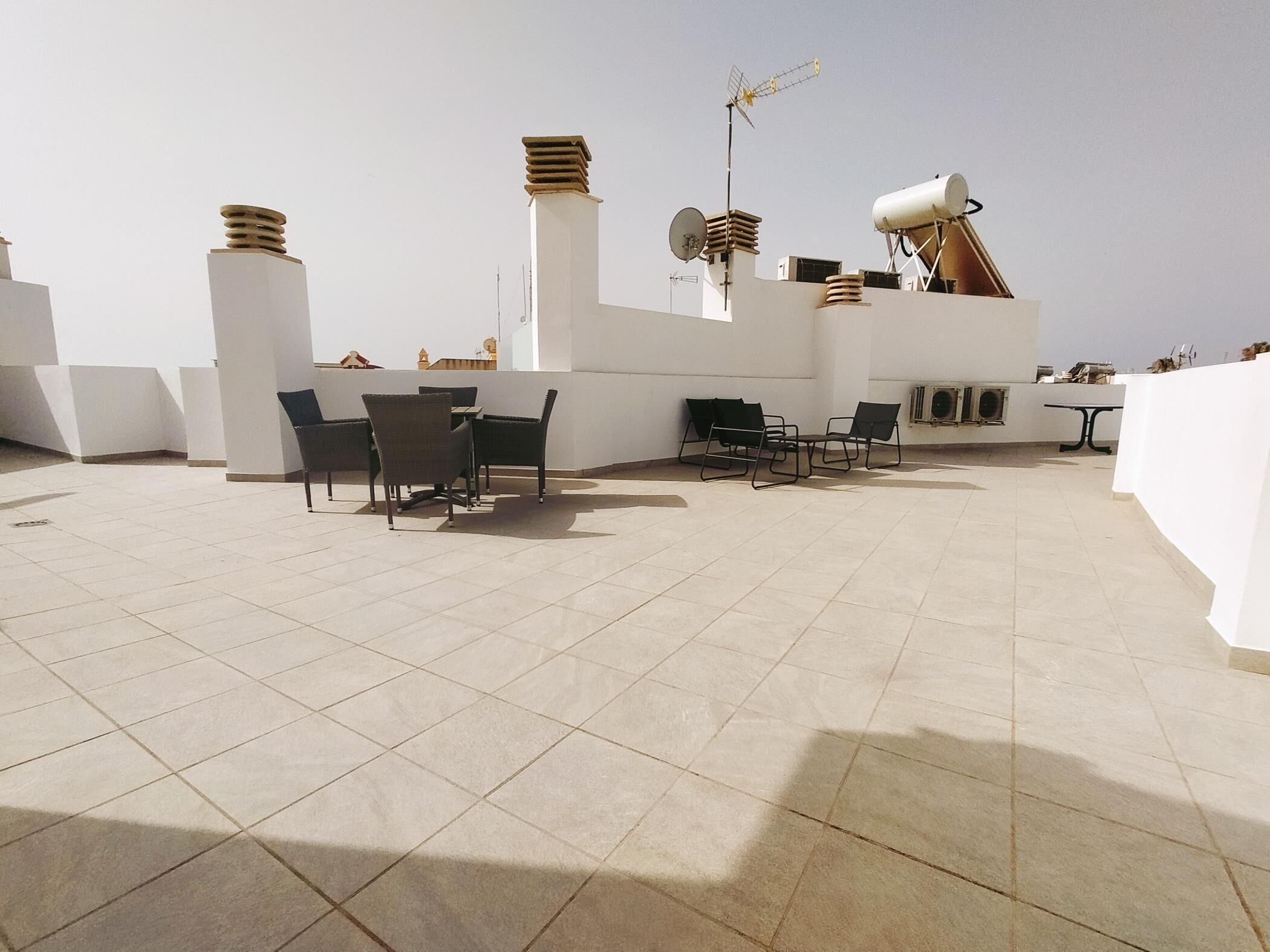 A rooftop terrace with tiled flooring, outdoor seating, and a satellite dish.
