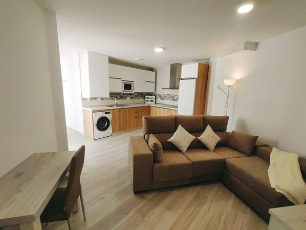 Een moderne woonkamer met een bruine modulaire bank, een eettafel met stoelen, en een keuken op de achtergrond.