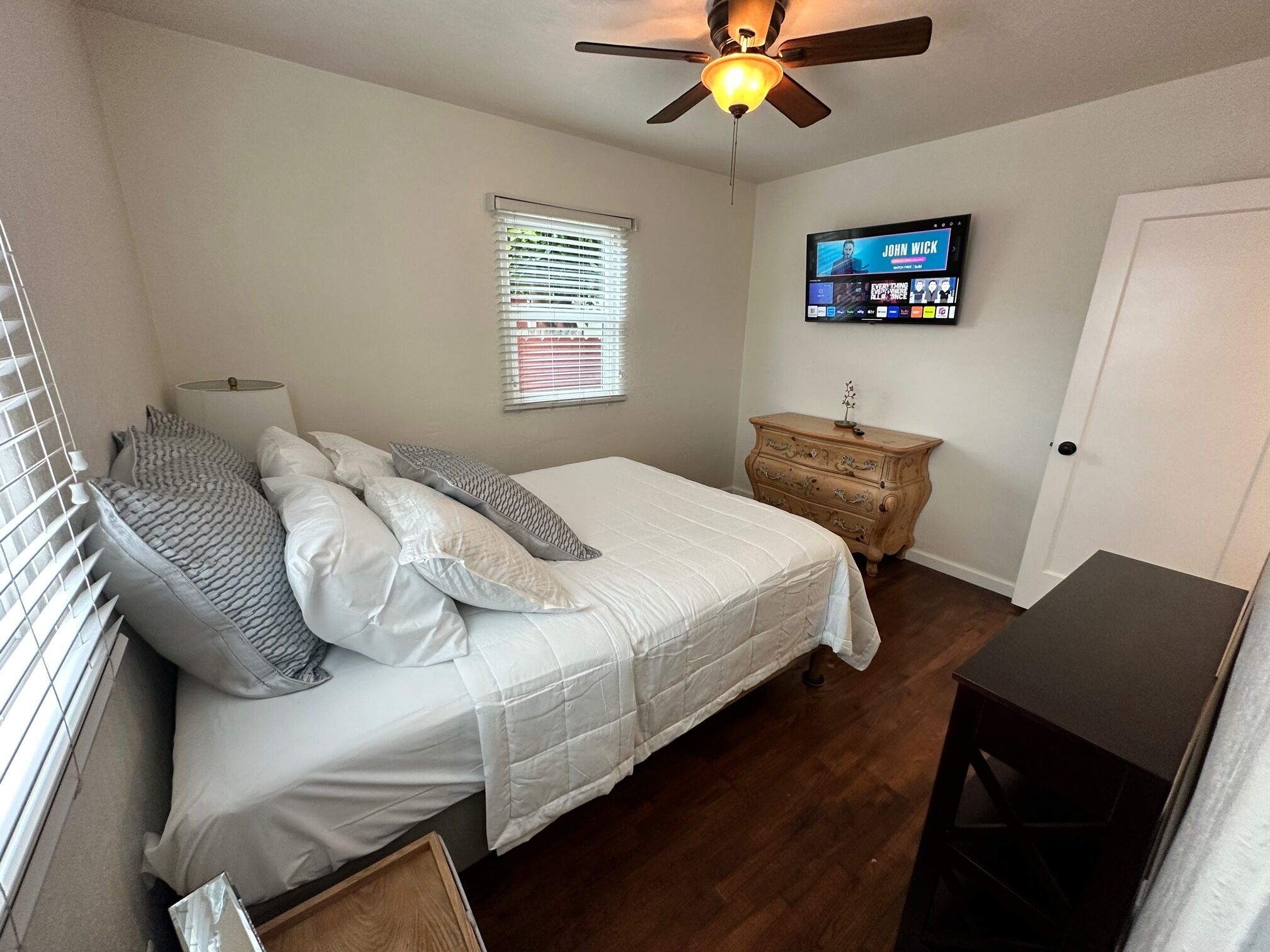 Une chambre à coucher comprenant un lit, une commode, un téléviseur fixé au mur et un ventilateur de plafond.