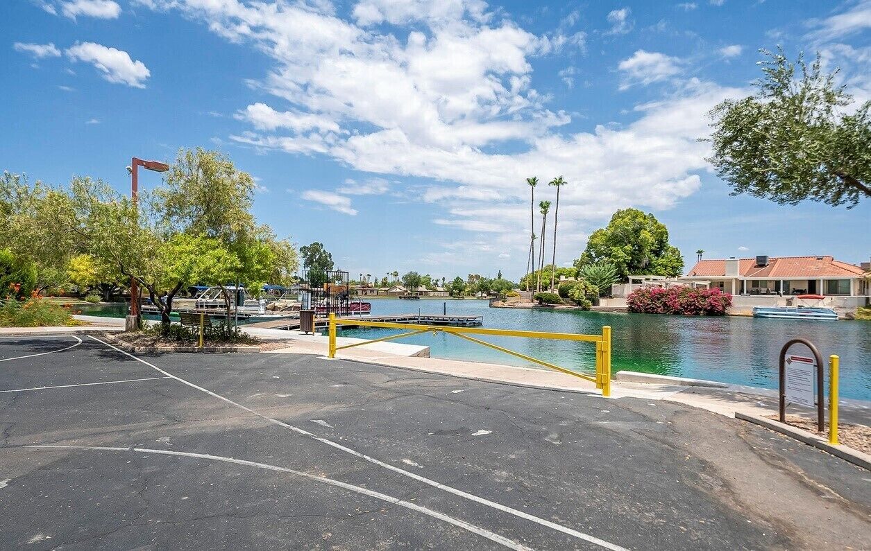 A parking area with a pool and a bridge over water, surrounded by trees and a building with a red roof.