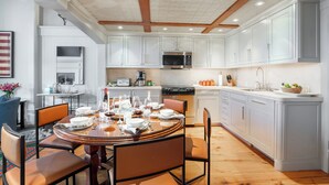 Une cuisine moderne avec des meubles blancs, un îlot central et un coin repas comprenant une table ronde et des chaises.