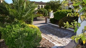 A paved pathway leading to a building with a tiled roof, surrounded by lush greenery and a white wall. - Casa Oslo - L'Estartit, Torre Vella (Estartit (L´))