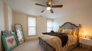 A bedroom with a bed, a nightstand, a bedside lamp, a ceiling fan, and a window.