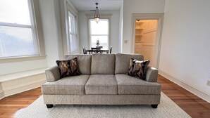 A spacious living room with a grey sectional sofa, a dining table with chairs, and a hallway leading to a closet.