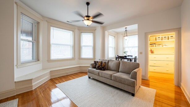 A spacious living room with hardwood floors, a grey sofa, and a ceiling fan.