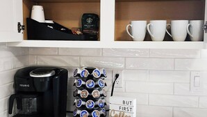 Keittiössä on Keurig-kahvinkeitin, kahvikapselihylly ja kyltti, jossa lukee: ”MUTTA ENNEN KAHVIA”.