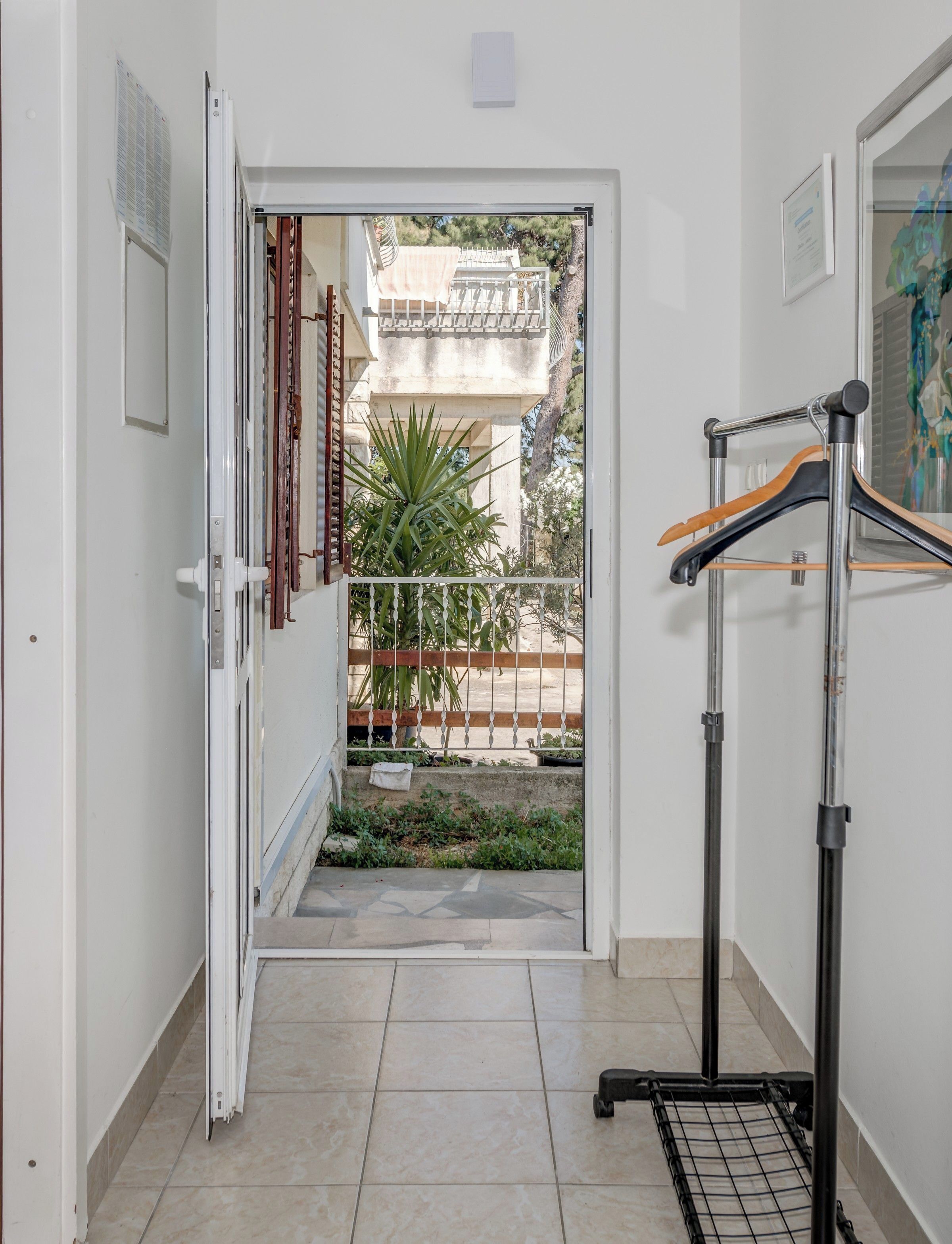 A corridor with a door leading to a balcony with a view of a building and a palm tree.