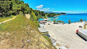 A coastal area with a parking lot, a small building, and a beach with clear blue water. - Beachfront apartment Drazen, with patio & parking (Split)