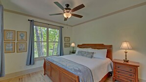 Une chambre à coucher avec un lit en bois, un ventilateur de plafond, une table de chevet avec une lampe et une fenêtre avec des rideaux.