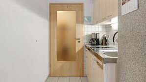 Una cocina con puerta de madera, un lavamanos, armarios y una cafetera.
