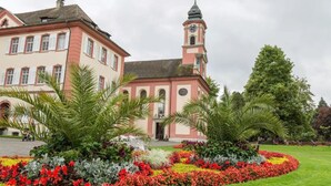 Un edificio histórico con una torre de reloj, rodeado de un jardín bien cuidado con diversas plantas y flores.