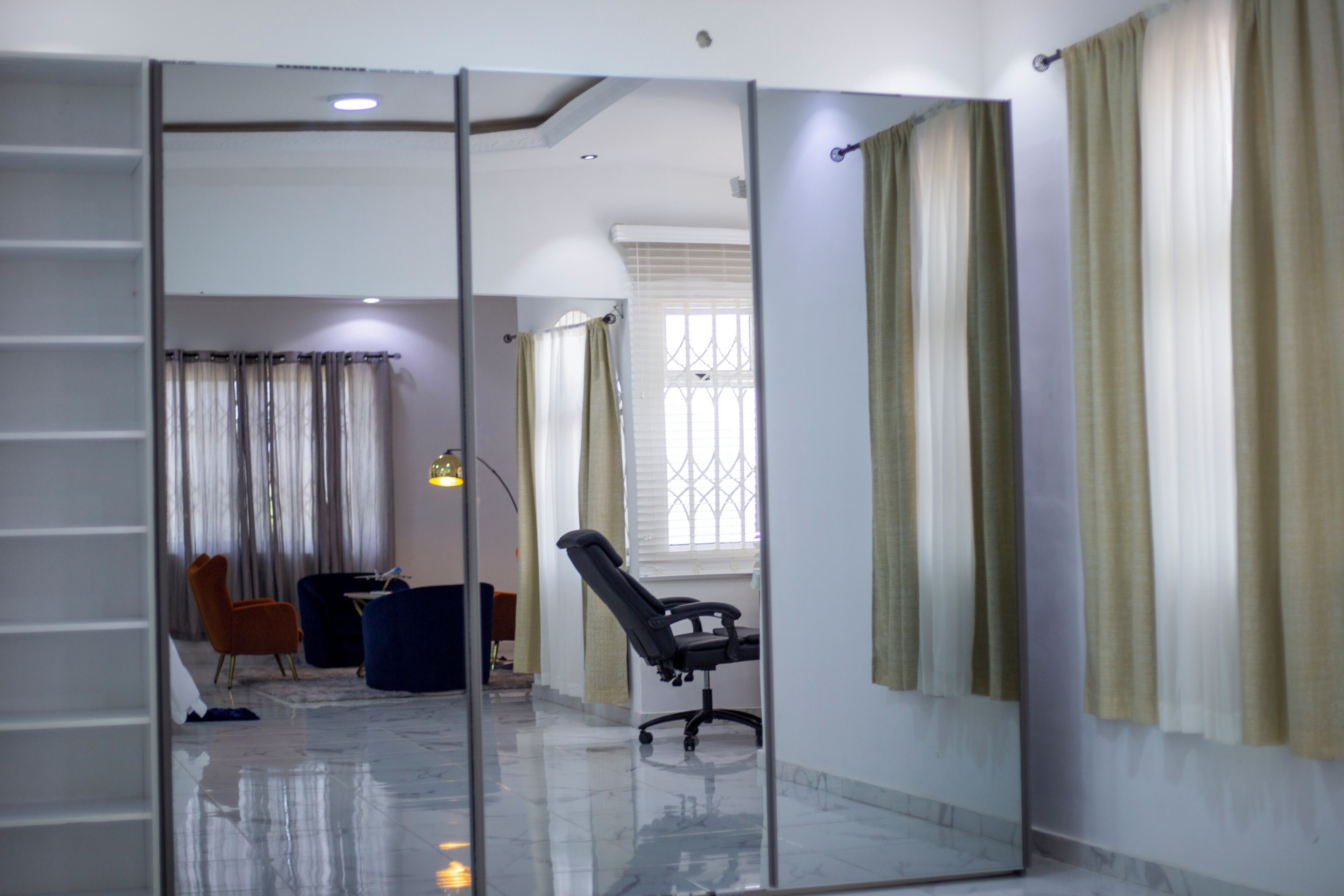 A modern office space with a glass partition, a black office chair, and a blue sofa.