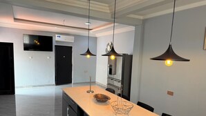 A modern kitchen with a marble countertop, pendant lights, and a black refrigerator.