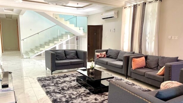 A modern living room with two sofas, a coffee table, and a staircase in the background.