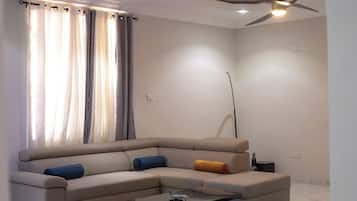 A modern living room with a beige sectional sofa, a glass coffee table, and a ceiling fan.