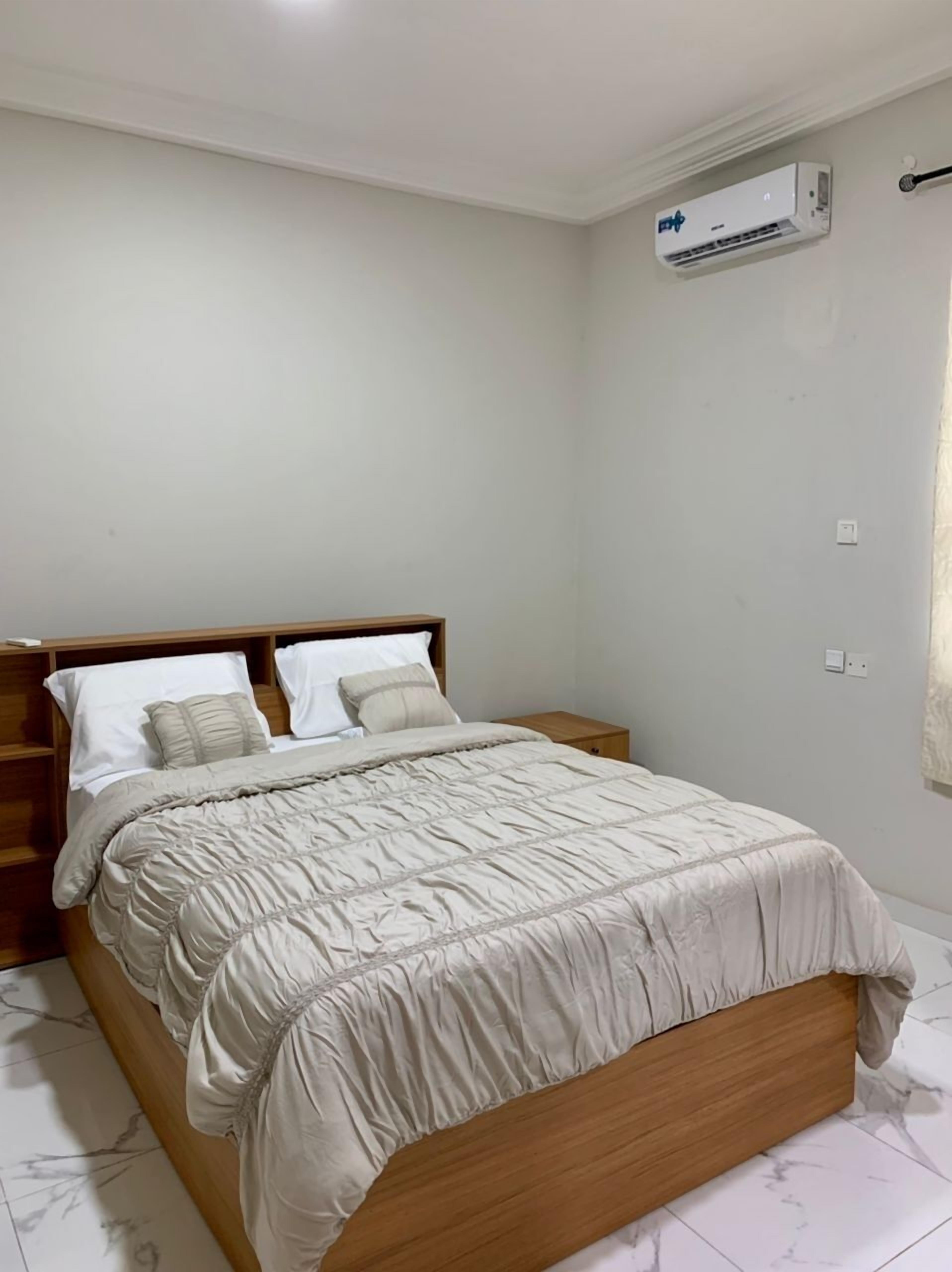 Ein Schlafzimmer mit einem Bett, einem Holzkopfteil, Nachttischen, einer Wand-Klimaanlage und einem Lichtschalter.