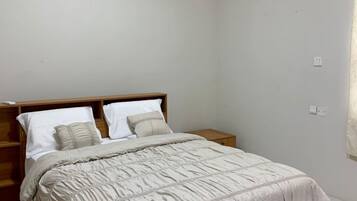 Ein Schlafzimmer mit einem Bett, einem Holzkopfteil, Nachttischen, einer Wand-Klimaanlage und einem Lichtschalter.