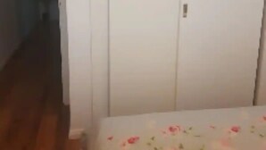 Et soveværelse med en seng dækket af et blomstret sengetæppe, en hvid garderobe og trægulv.