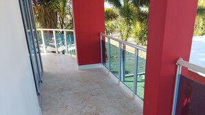 Un couloir au sol carrelé, aux murs rouges et doté d’une rambarde en verre donnant sur un jardin.