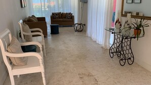 Un salon avec un sol carrelé de couleur beige, des meubles blancs et bruns, une table basse en verre et une plante en pot.