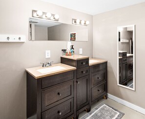 A bathroom with two sinks, dark wooden cabinets, a mirror with lights, and a rug on the floor. - 6bd 3ba large gathering home, close to YMCA and 5 miles to Downtown Duluth (Hermantown)