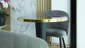 Un interior moderno con una mesa redonda, una silla tapizada de gris y una planta en maceta con flores.