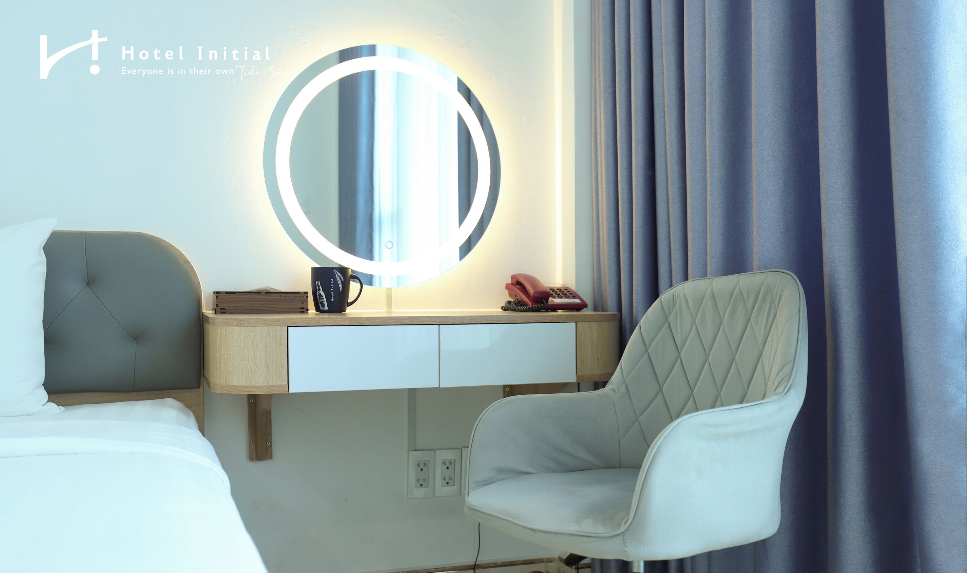 A hotel room with a bed, a desk with a mirror, a chair, and a telephone.
