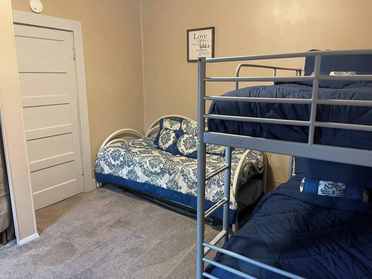 Une chambre avec un lit superposé, une porte, une citation encadrée au mur et une couvre-lit à motifs.